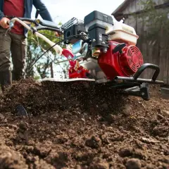 Mężczyzna z glebogryzarką spulchnia ziemię. To pielnik do glebogryzarki, który ułatwia pracę w ogrodzie.