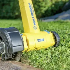 Żółta obcinarka do krawędzi trawnika z obrotową szczotką, pracująca na trawniku przy betonowym obrzeżu.