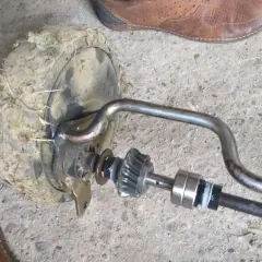 Zestaw naprawczy przekładni napędu kosiarki z zabrudzonym kołem i elementami mechanizmu.