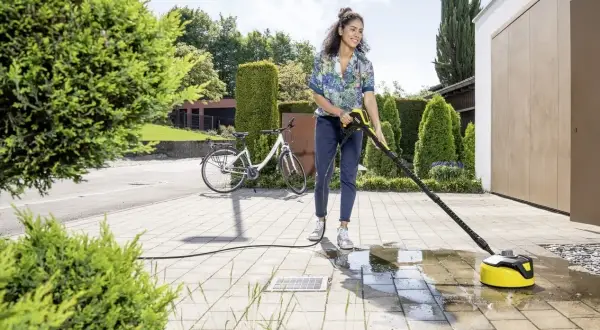 Kobieta używa maszyny do mycia kostki brukowej, aby oczyścić podjazd.
