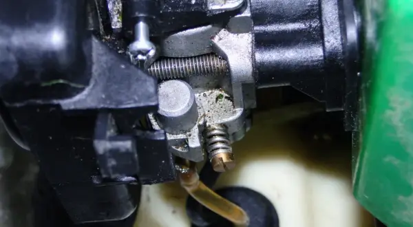 Zbliżenie na gaźnik do kosy spalinowej, widoczne elementy metalowe i plastikowe, przewód paliwowy.