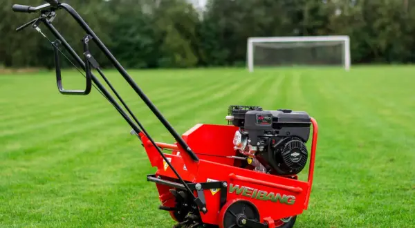 Czerwony aerator Weidemann na trawniku. Urządzenie to służy do napowietrzania gleby, poprawiając jej strukturę i zdrowie trawy.