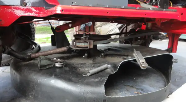 Podczas naprawy traktorka, widać mechanizm kosiska z pasem napędowym i sprężyną.