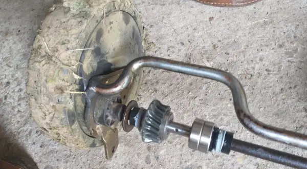 Zestaw naprawczy przekładni napędu kosiarki z zabrudzonym kołem i elementami mechanizmu.